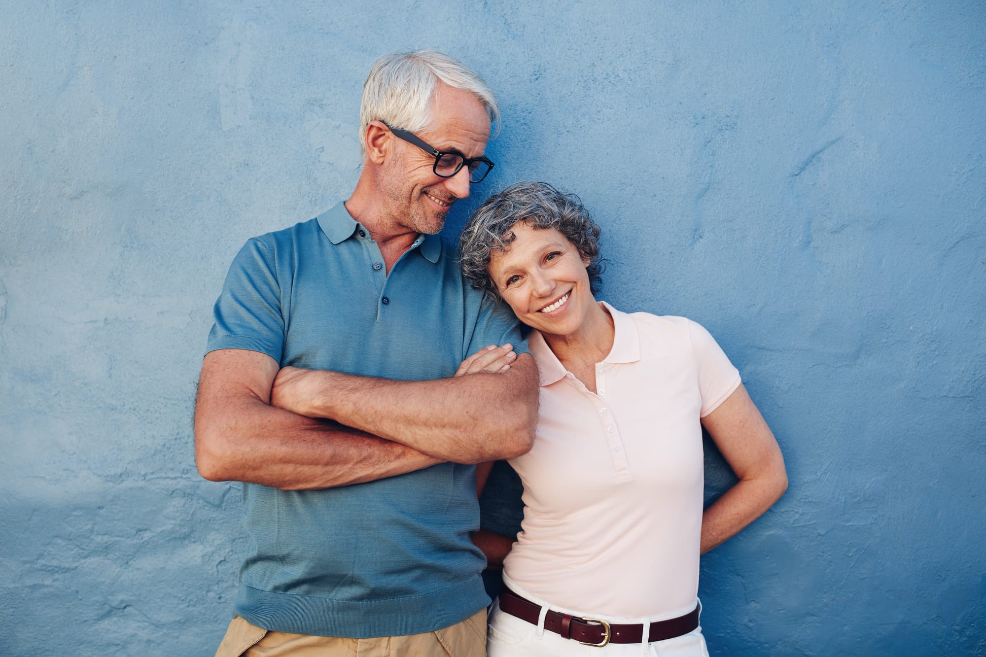 A retired couple smiling together against a blue wall